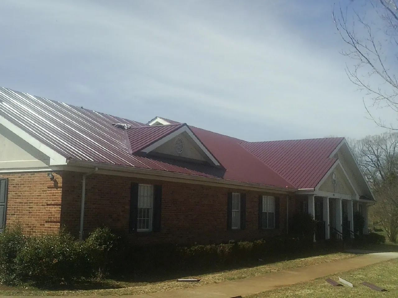 Red metal roof with gabled entries on a long brick building, from a Hail Damage Roof Repair job in Montague