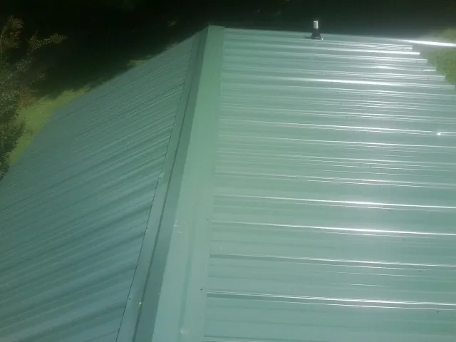 New green metal panels meeting at the ridge of a roof — Flat Roof Repair work by our crew in Montague