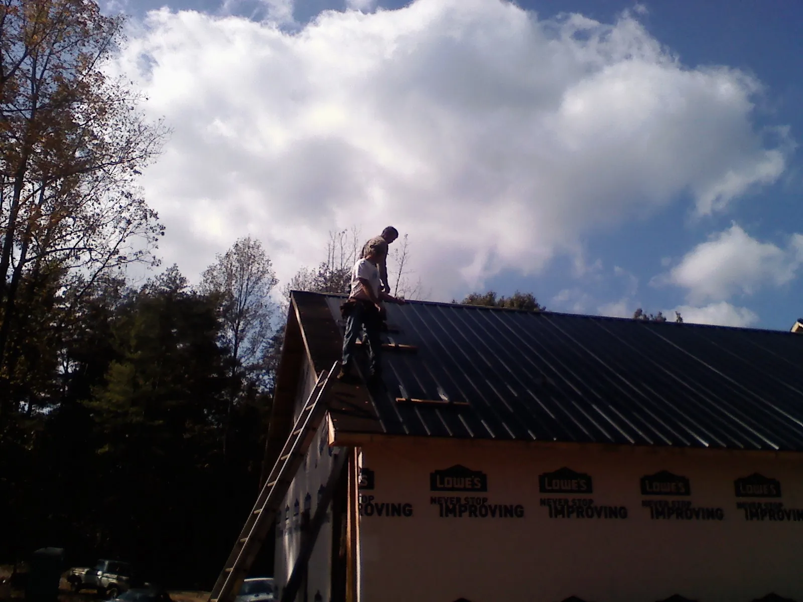 Roofer fastening dark metal panels high against a cloudy sky, from a Roof Inspection job in Montague
