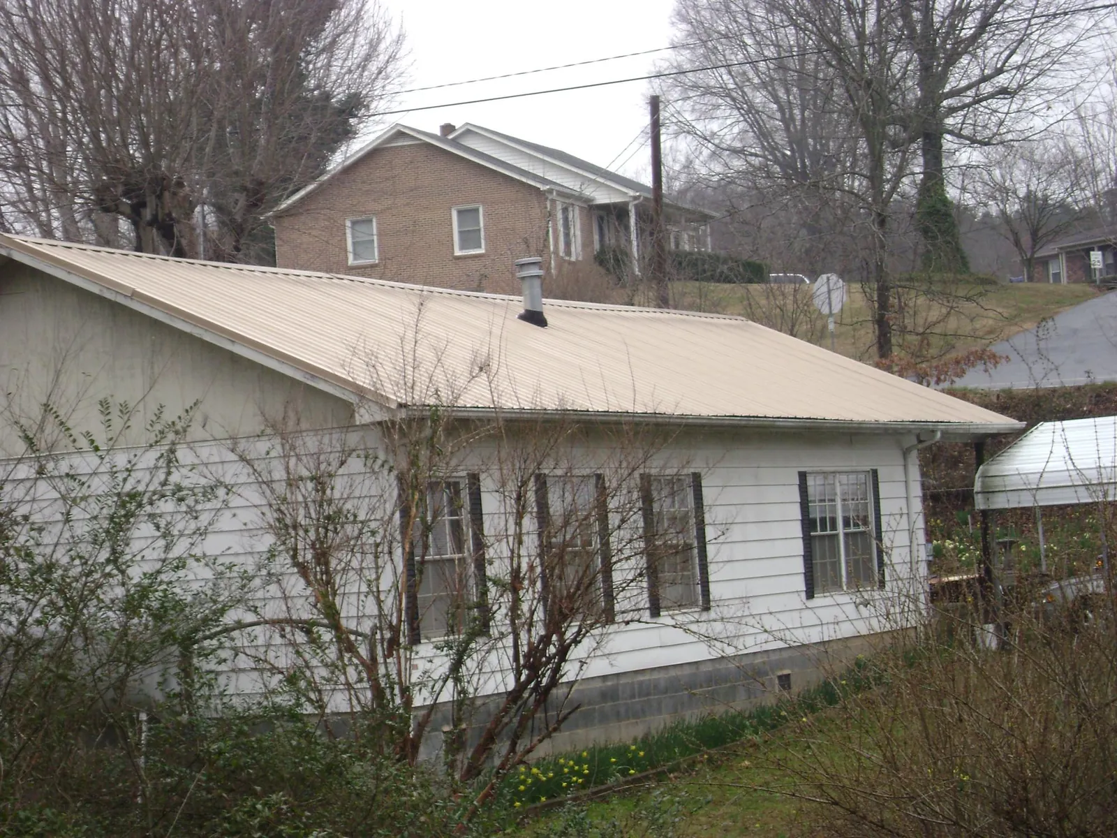 Tan metal roof on a white sided house set into a hillside — Commercial Roofing by Roofing Brothers in Montague